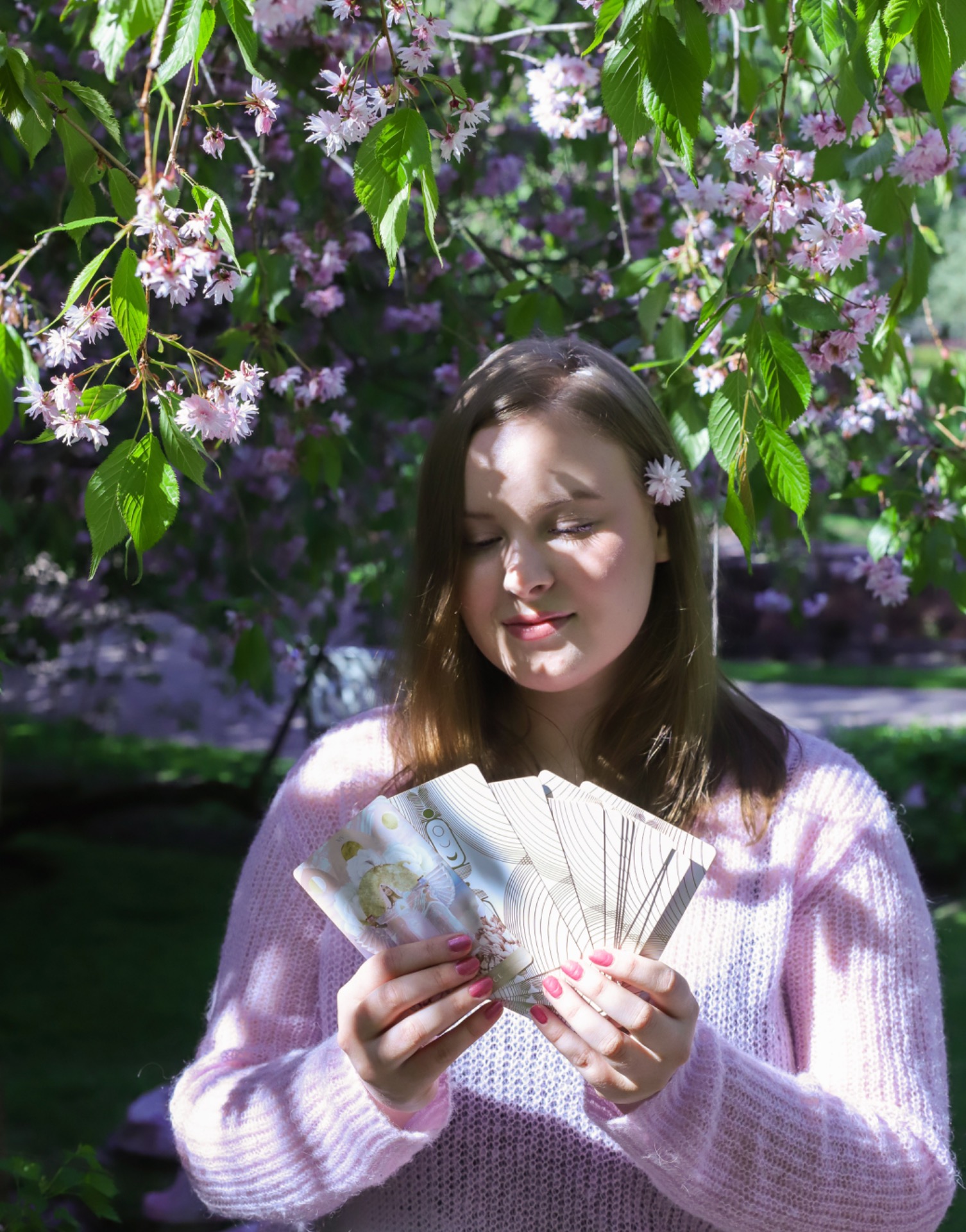 Violetilla liinalla tarotkortteja, peilin heijastus ja vaaleanpunaisia kukkia. Mainos Ainon tekemille tarot-tulkinnoille Helsingissä.